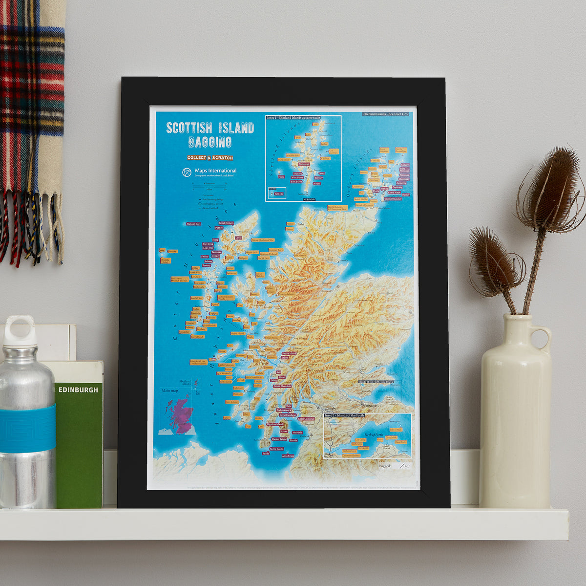 A framed Scottish Island Harumo map print displayed on a white shelf in a styled interior setting with a bottle, books, and a vase.